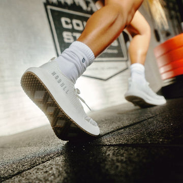 Person wearing white sneakers with a brand logo on a blurred background